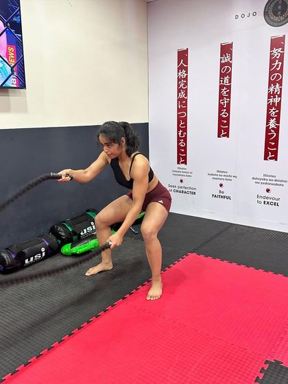 A female student builds her upper body and core strength with battle ropes, a staple in our high-intensity conditioning circuits.