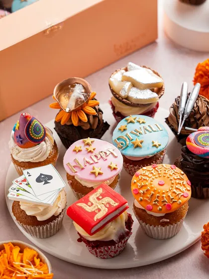 A box of twelve mini cupcakes, each with a unique Diwali-themed topper, including playing cards, diyas, and festive greetings. These are perfect for parties and sharing the festive joy in bite-sized form.