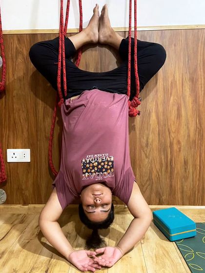 A student practices a supported headstand variation using the wall ropes. This inversion builds confidence and strength while ensuring the neck remains safe and supported.