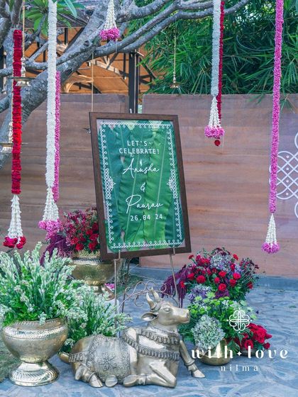 The welcome area for a summer wedding, with a custom sign, brass decor, and hanging floral garlands.