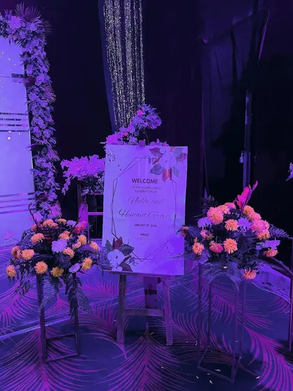 The welcome area for an anniversary celebration, where we used dramatic purple lighting to highlight the floral arrangements and personalized sign.