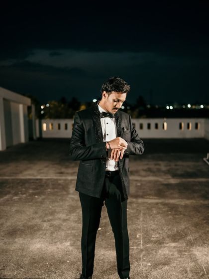 The groom adjusting his cufflink, a classic and stylish shot taken on a rooftop at night.