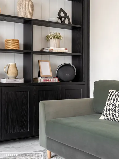 In the Sunlit Serenity living room, a deep green sofa sits beside a custom black display unit. We love using built-in furniture to create a sense of permanence and provide beautifully styled storage.