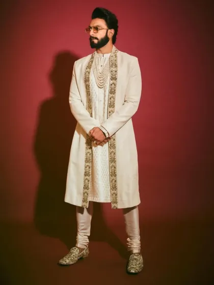 A celebrity-inspired look perfect for a grand wedding. This ensemble features an ivory sherwani with intricate gold embroidery, paired with a matching kurta, churidar, and a multi-layered pearl necklace for a truly regal appearance.
