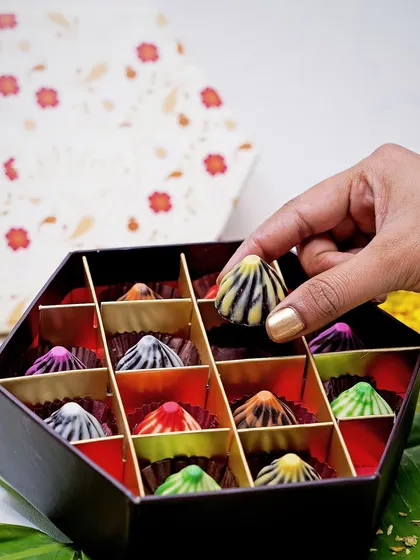 A hand selecting a colorful chocolate modak from a festive gift box. This shot captures a traditional sweet with a modern twist, perfect for festival-themed marketing for Ganpati Chaturthi.
