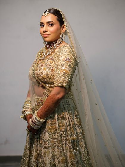 A full-length view of the bride in her ivory and gold lehenga. The entire look is one of timeless elegance, a style many modern brides desire.