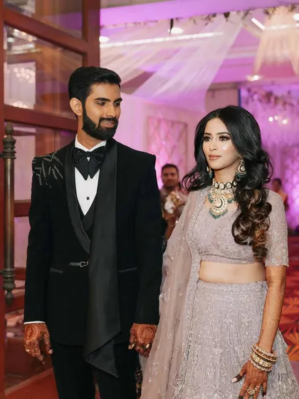 A beautiful couple at their reception. The bride's makeup is soft and romantic, with a focus on a flawless complexion and defined eyes that complement her elegant lavender lehenga.
