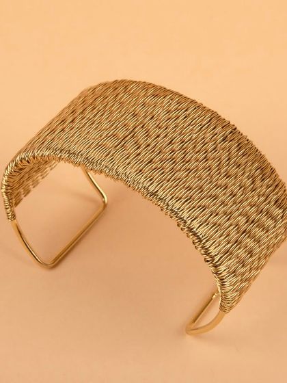 An angled, high-contrast shot of the woven gold cuff.