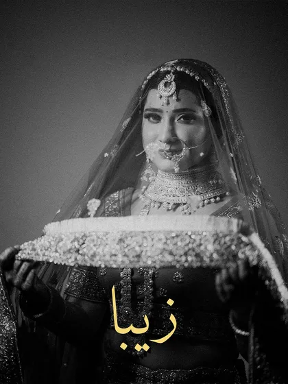 A timeless black and white portrait of the bride. The name "Zeba" is elegantly written, and the focus is on her holding the edge of her veil, creating a classic, poignant look.