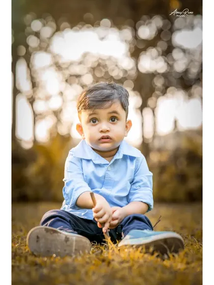 A beautiful, warm-toned portrait of Ivaan sitting in the grass. The soft, out-of-focus background makes his curious expression the center of attention in this outdoor shot.