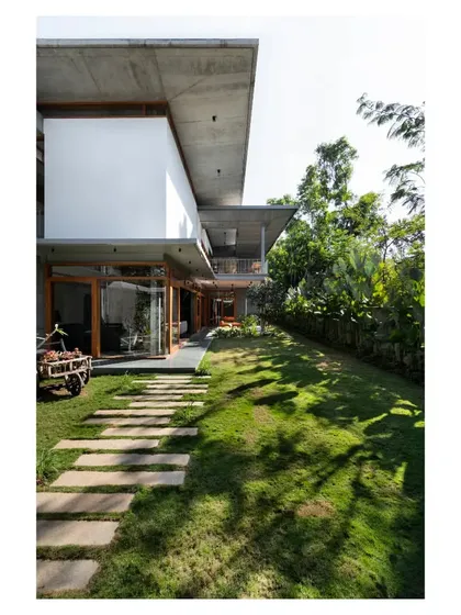 The House of Canopies, where bold cantilevered concrete roofs provide shelter while framing views of the garden. A simple stone path set in the lawn blurs the line between the built structure and the landscape, inviting the outdoors in.