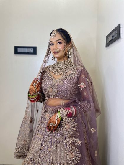 A beautiful reception bride in a lavender lehenga. Her hair is styled in a soft updo with a maang tikka, creating a dreamy and romantic look.