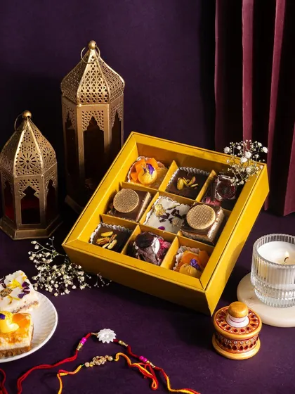 A beautiful gift box of assorted mini cakes. The moody, dark background with a glowing lantern creates a sense of premium, after-dark indulgence.