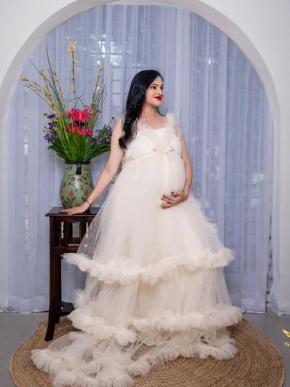 A solo portrait of the mother-to-be in a stunning, multi-layered tulle gown. The arched window and floral arrangement create an elegant and classic studio look.
