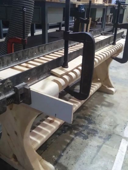 A student-made bench is held in a large clamp during the glue-up process, ensuring tight joints and a strong final structure.