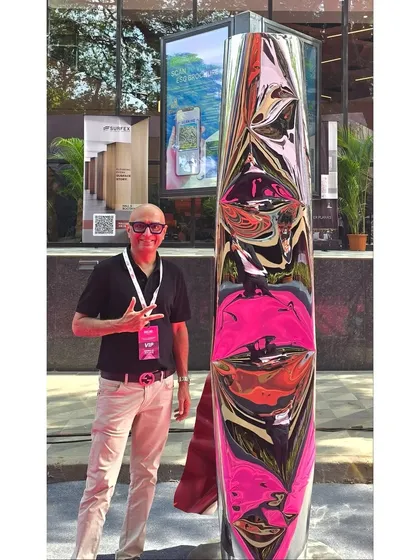 Standing with my sculpture "Eternal Grace" at the Acetech exhibition. The piece reflects the vibrant colors of its surroundings.