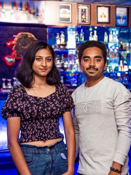 A couple standing in front of my well-stocked bar. The blue backlighting creates a cool, modern vibe, perfect for a night out in Bangalore.