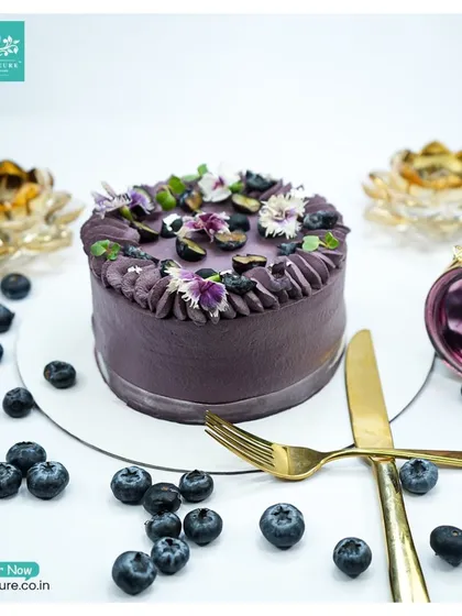 Our Blueberry Cake, styled with scattered fresh blueberries and elegant gold cutlery, ready to be served.