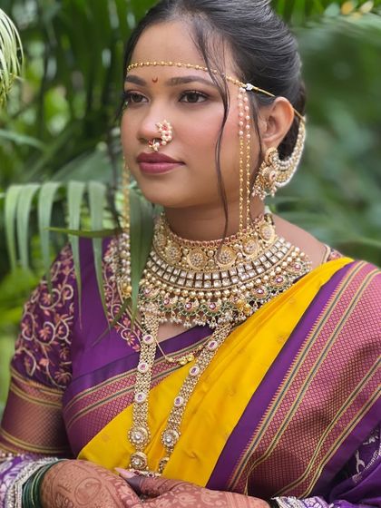 A regal Maharashtrian bride adorned in traditional jewelry. The makeup features a neutral palette with a slight shimmer on the eyes to let the heavy jewelry and bright saree shine.