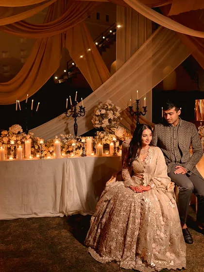 The couple shares a quiet moment amidst the warm glow of their sangeet. The backdrop of flowing drapes and a table laden with candles created a perfectly romantic and photogenic setting.