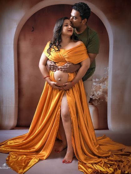 A warm and loving couple's portrait. The father-to-be kisses his partner's head as they both cradle the baby bump, dressed in a beautiful golden-yellow satin gown.