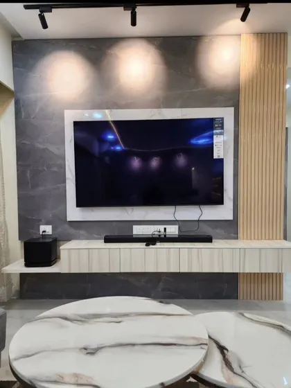 A modern living room with a large TV mounted on a grey marble-effect wall. Track lighting on the ceiling provides flexible and focused illumination.
