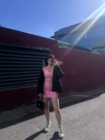 A bright pink vinyl co-ord set with a crop top and mini skirt, layered with a black blazer for an edgy look.
