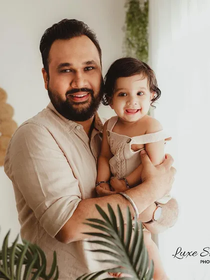 A proud father holds his smiling baby. This portrait captures the special bond between a dad and his child in a warm, natural light setting.