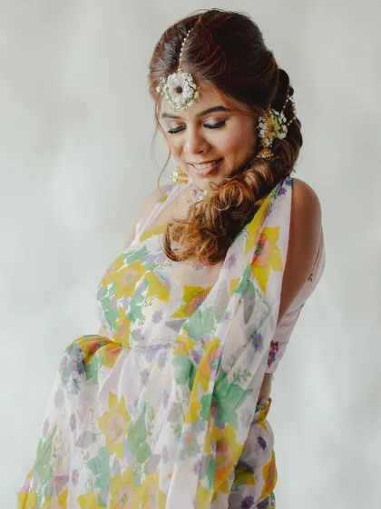 A bride looking serene, wearing a floral maang tikka and hairpiece.