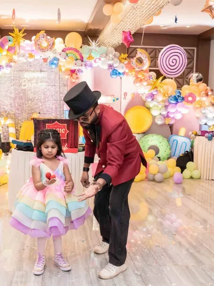 The birthday girl, dressed in a beautiful rainbow dress, helps me with a classic sponge ball trick. Her focus and delight are what make these moments so precious.
