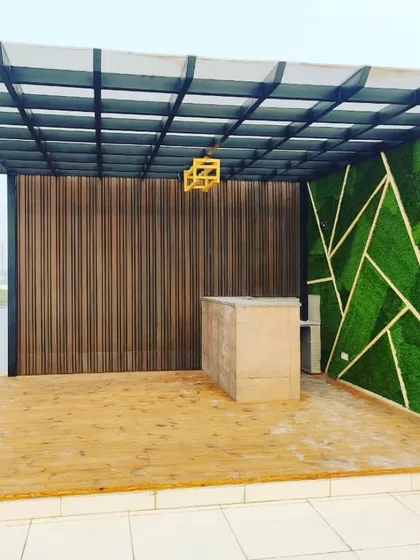 A beautiful pergola with a thermopine wood deck. The back wall features WPC louvers and a geometric green panel, with a bar counter ready for finishing.