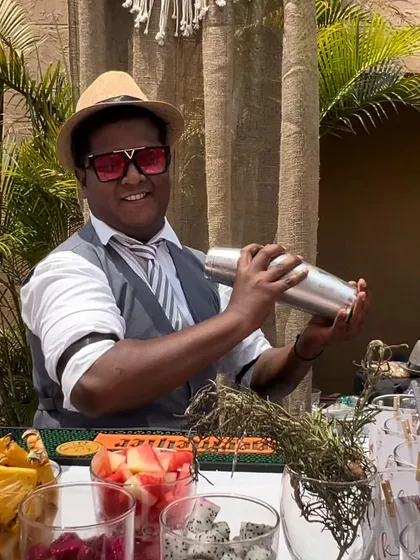 One of our bartenders in action, shaking up a fresh, fruity cocktail at a sundowner event. The bar is stocked with a colorful array of fresh-cut fruits like strawberries and dragon fruit.