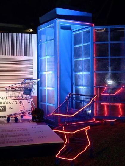A creative installation for a travel-themed party, with a telephone booth, neon-lit luggage carts, and a giant boarding pass prop.