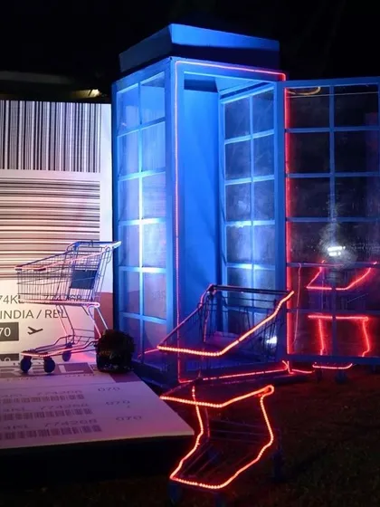 A creative installation for a travel-themed party, with a telephone booth, neon-lit luggage carts, and a giant boarding pass prop.