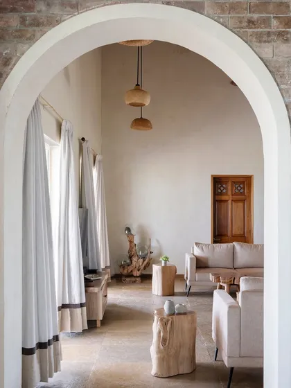 An arched view into the main living area, highlighting the use of natural materials like the log side tables and the soft, neutral tones of the furniture.