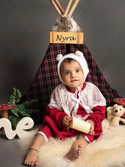 A cozy, camp-themed first birthday shoot. This little girl is dressed in red and sitting in front of a teepee with woodland props.