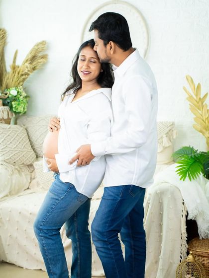 A tender moment in our casual studio setup. The partner kisses his partner's forehead as they both cradle the baby bump, dressed in relaxed jeans and white shirts.