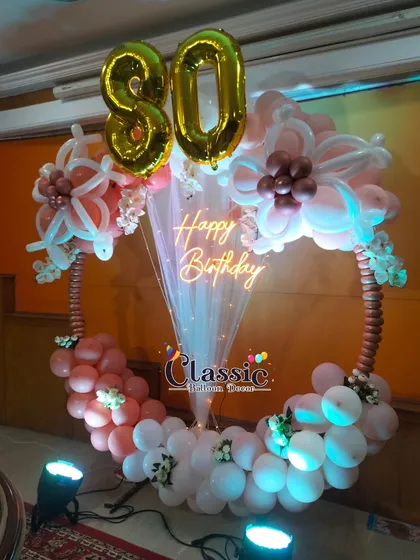 An elegant and unique 80th birthday ring decoration. We used a mix of balloon twisting and arranging techniques to create floral shapes on a hoop, complemented by a 'Happy Birthday' neon sign and large '80' foil numbers.