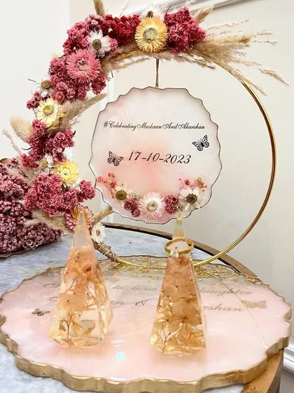 A beautiful ring platter in shades of pink and peach, with pyramid ring holders containing preserved hydrangeas. The floral hoop is decorated with dried flowers and pampas grass.