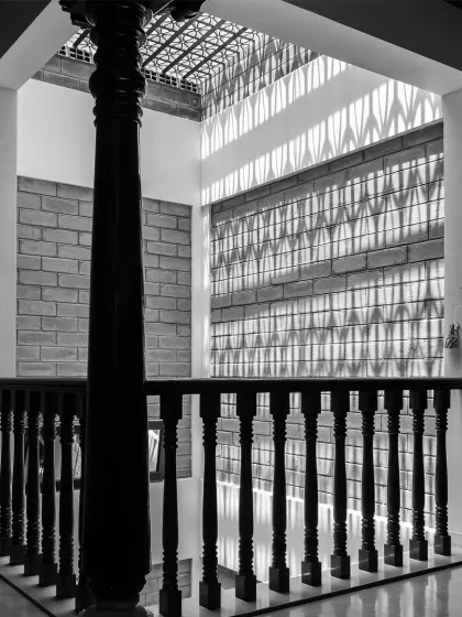 A black and white photograph capturing the dramatic interplay of light and shadow created by a skylight and jaali screen, framed by a traditional pillar.