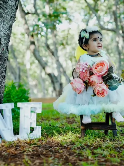 A fairy-tale first birthday. Dressed as a little angel, she sits among the trees, creating a truly magical and serene portrait for her milestone celebration.