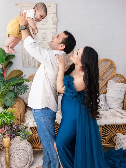 A moment of pure joy and connection. The father lifts his baby high, sharing a look of love, while the mother, in a stunning royal blue gown, watches on.