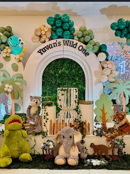 The full stage for "Yuvan's Wild One" birthday. This setup features a mix of plush and prop animals like elephants, zebras, and tigers, set against a backdrop with a lush green archway.
