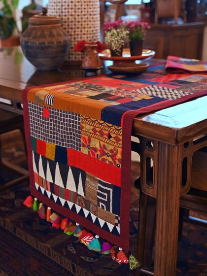 The autumn-colored scrap throw styled on a dining table. The piece is finished with machine stitching, hand stitching, and quirky appliqué details.