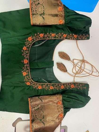 A dark green blouse with orange floral embroidery along the square neckline. The puff sleeves are made with a traditional gold border fabric.