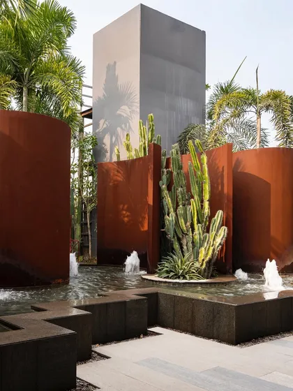 A sculptural water feature at the KEUS commercial hub. The design contrasts the industrial feel of rust-hued Corten steel walls with the organic forms of cacti and the movement of water, creating a bold, avant-garde landscape.
