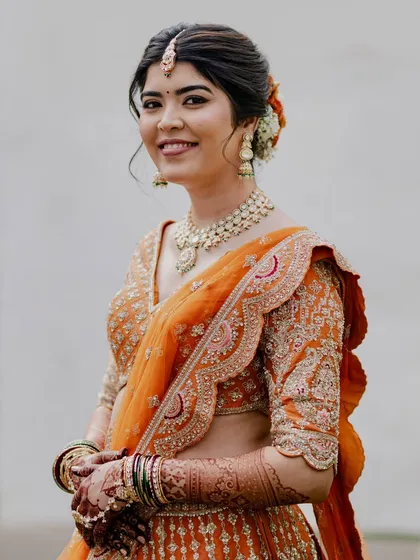 A smiling portrait of Reeya in her orange lehenga. The fresh, matte makeup look is perfect for an outdoor, daytime wedding ceremony.