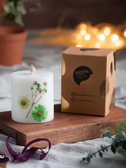This white pillar candle is decorated with real pressed baby's breath and green daisies. It's a simple, elegant design that brings a touch of nature indoors.