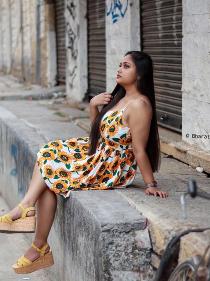A casual portrait on a city sidewalk. The sunflower dress adds a bright, cheerful element to the urban scene.