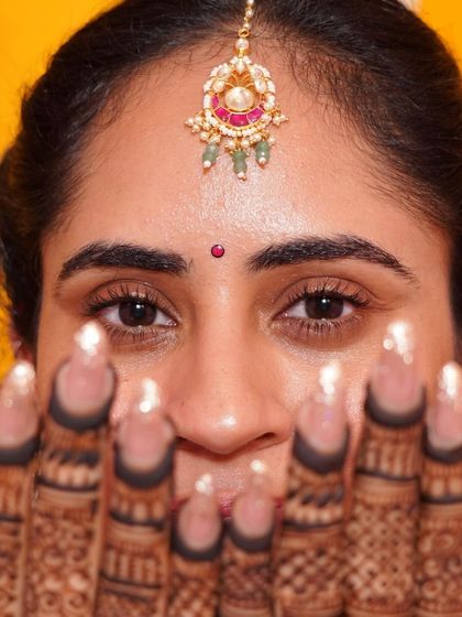 A close-up on the intricate details of a 'ghar wali mehendi'. The focus is on the beautiful henna design and the delicate maangtikka, showing how even simple accessories can elevate an intimate ceremony look.